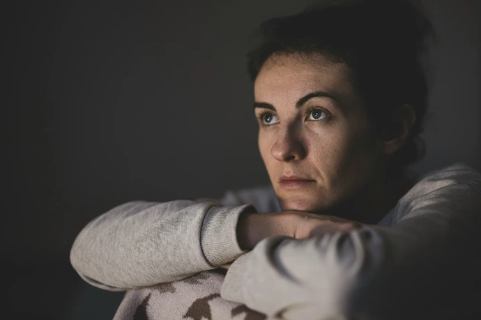 A woman with dark hair resting her chin on her hands in dim light